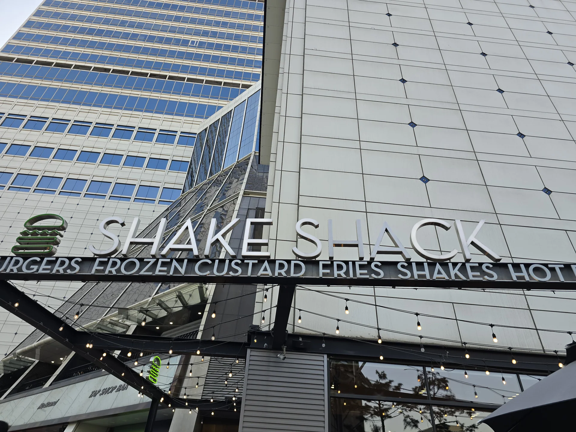 SHAKE SHACK 간판과 초록색 버거 로고 아래 여러 줄로 달린 전구