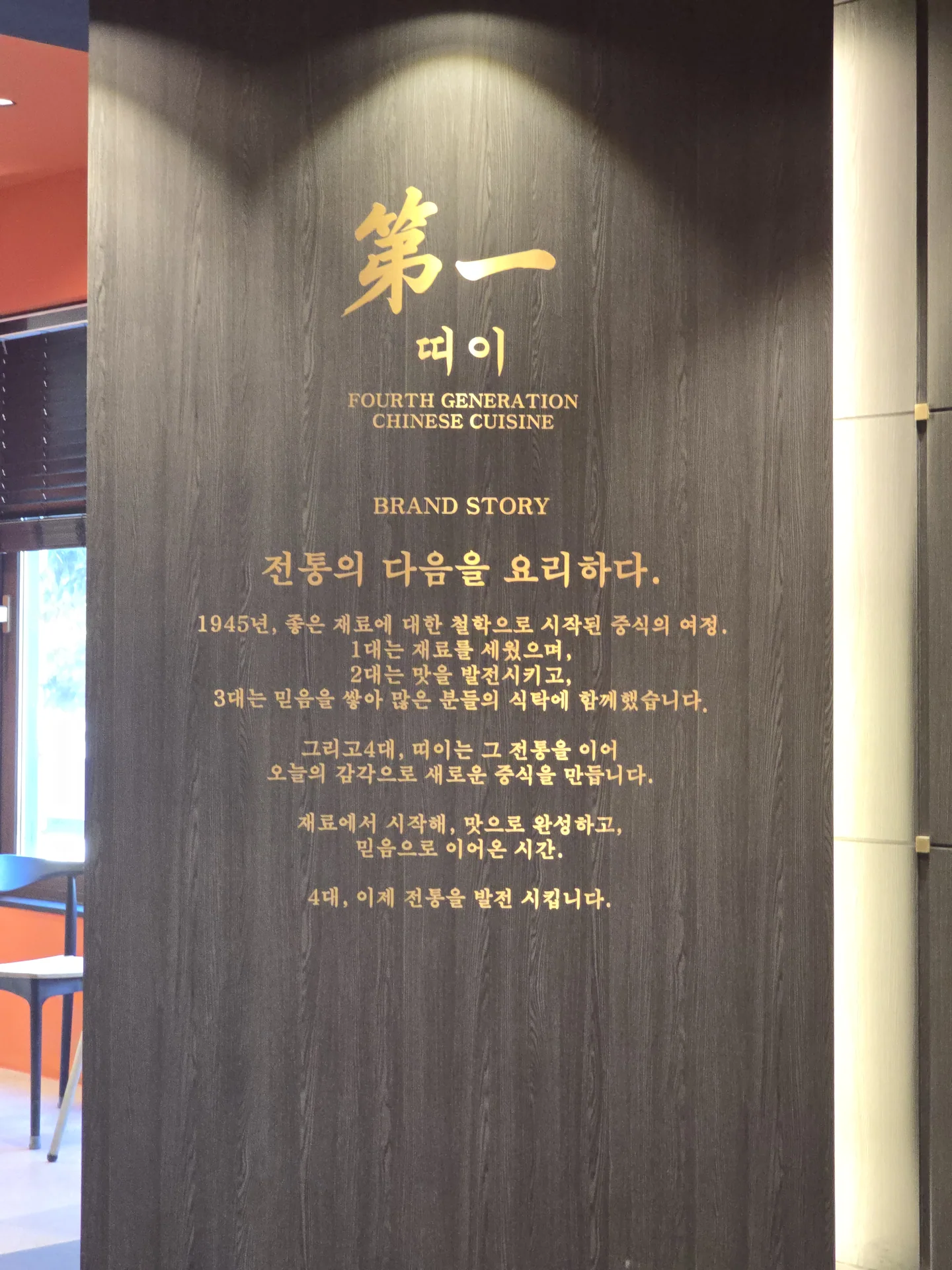 어두운 나무 무늬 벽에 금색으로 적힌 띠이 로고와 브랜드 소개